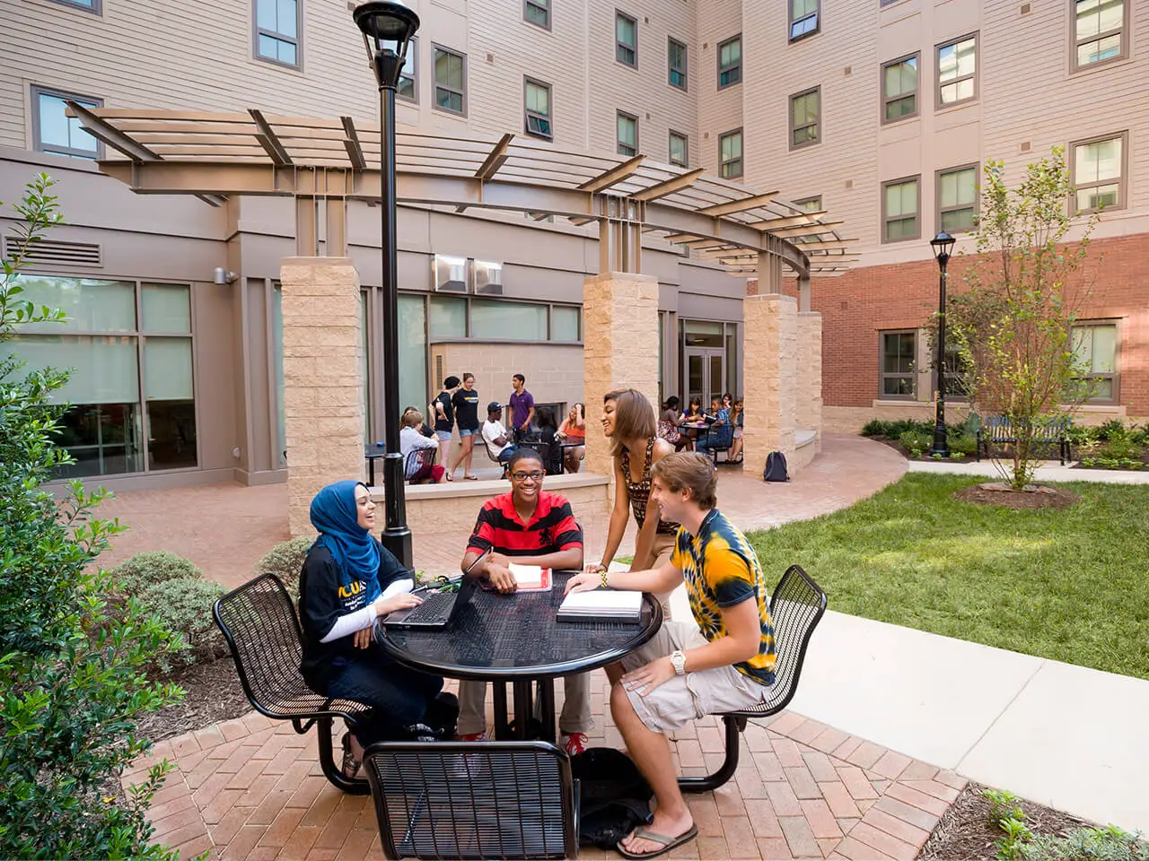 Students sitting at an outdoor table with laptops and books.