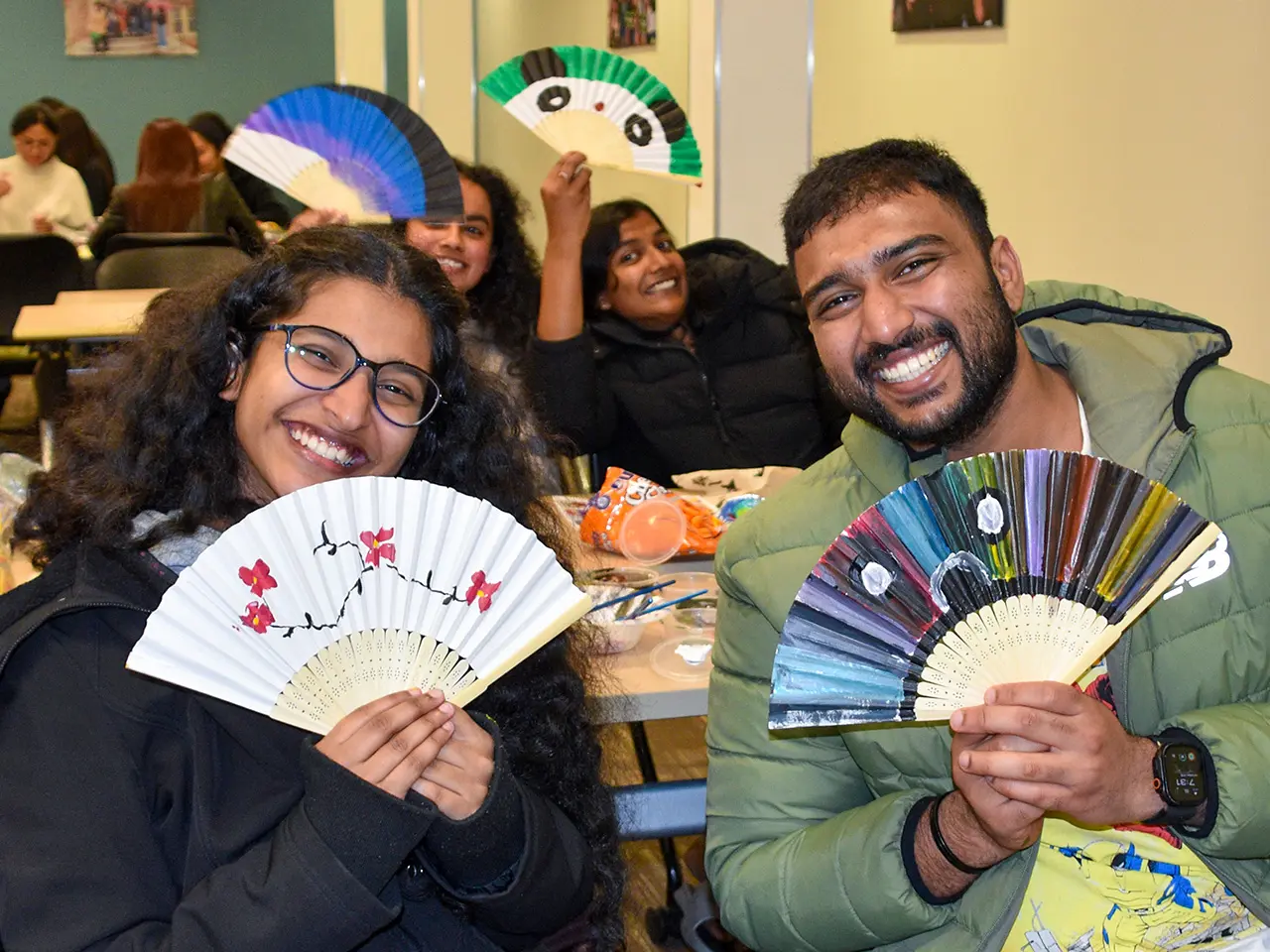A group holding up fans they hand painted at an international student event