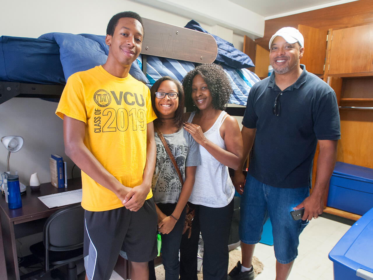 Family posing with a student in a dorm room