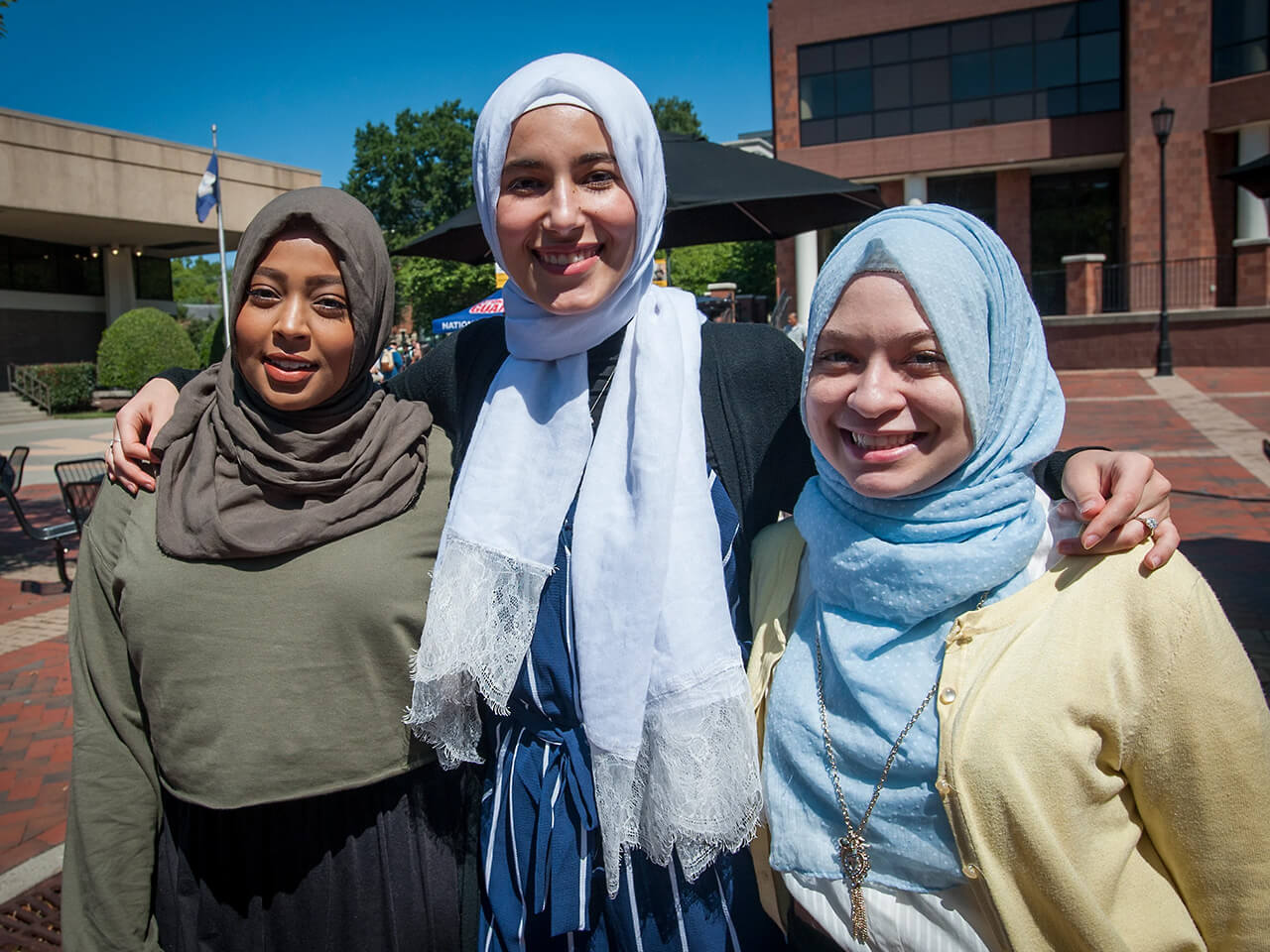 Three females with hijabs smile together outside