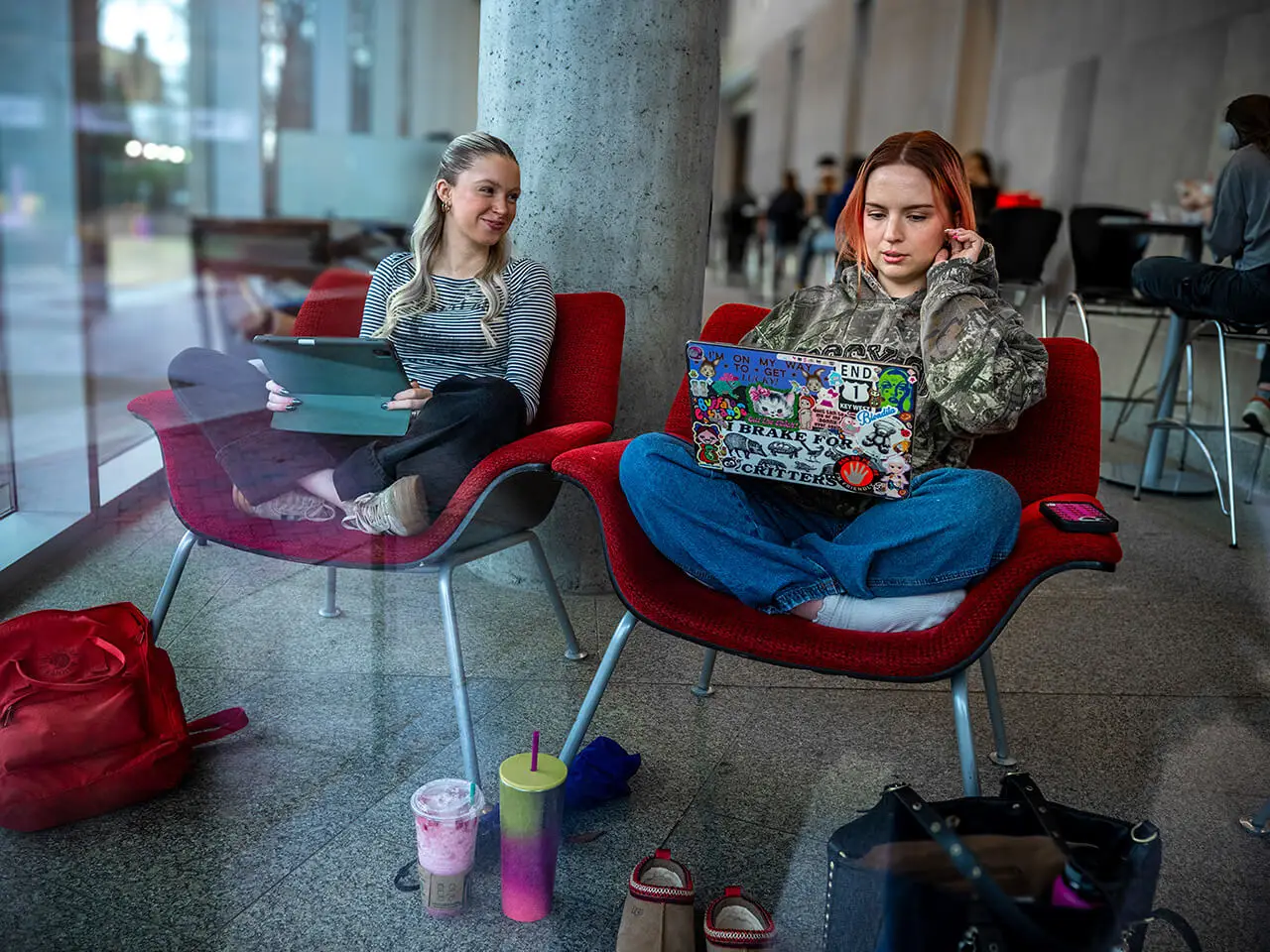 Two students sit surrounded by books and backpacks while studying