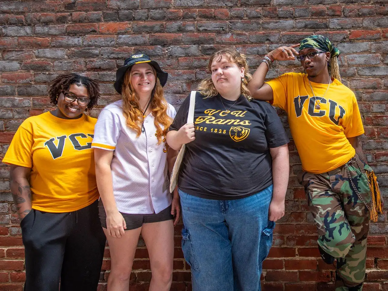 Four students wearing VCU black and gold clothing are standing against a wall facing the camera