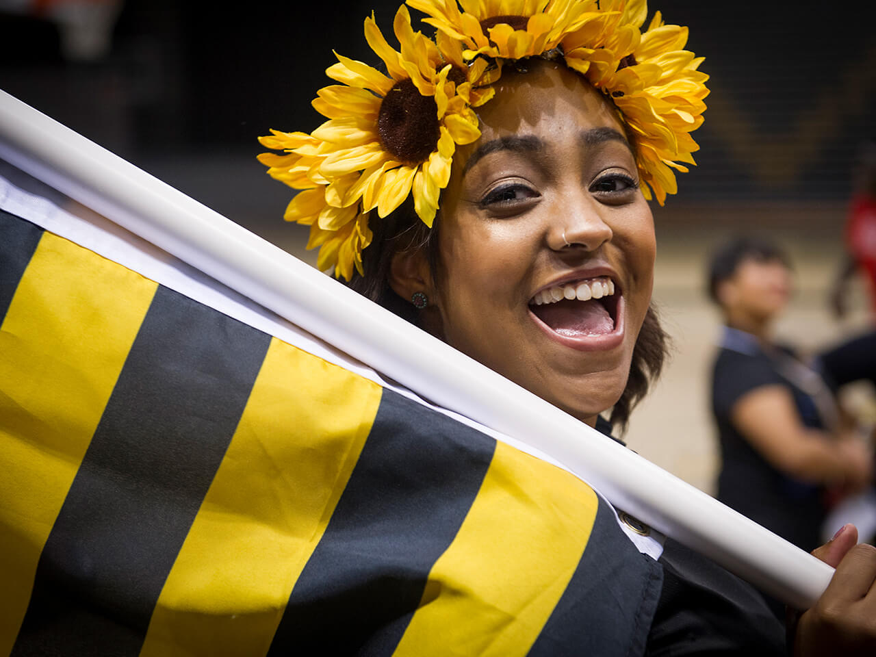 Student with flowers in her hair holding a gold and black flag